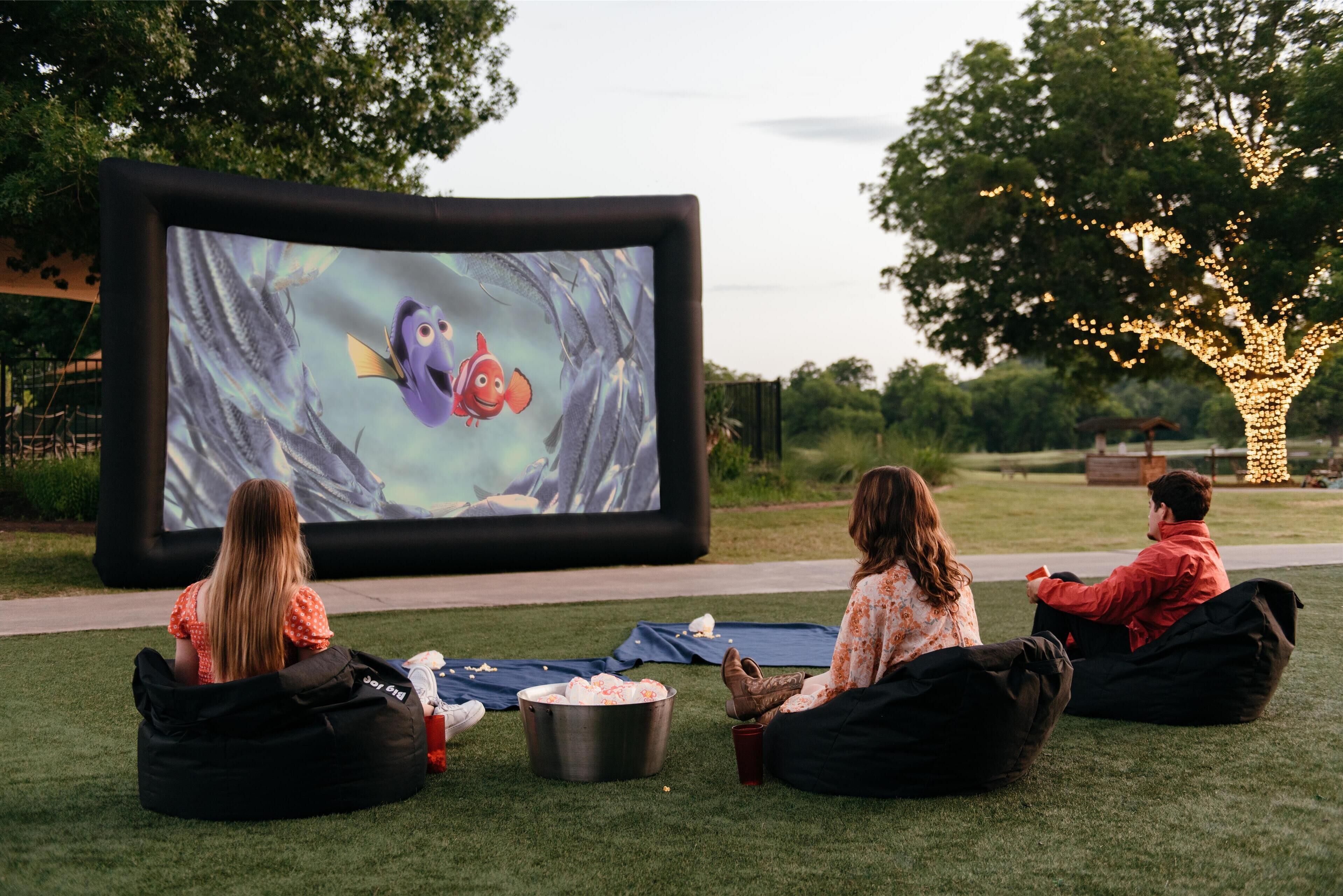 Trois personnes sont assises sur des poufs, regardant un film sur un grand écran installé à l’extérieur.
