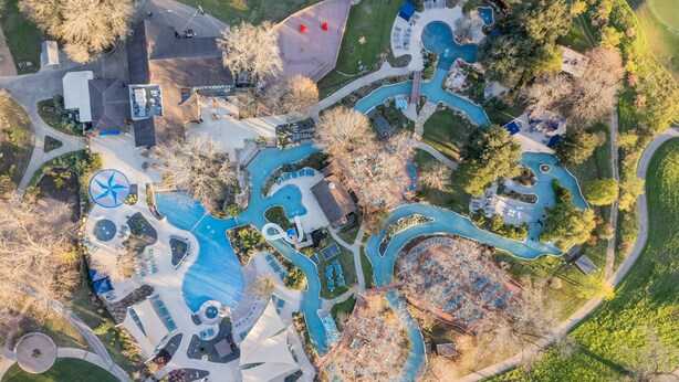 An aerial view of a resort with multiple swimming pools, a large wind turbine, and a variety of outdoor seating areas.