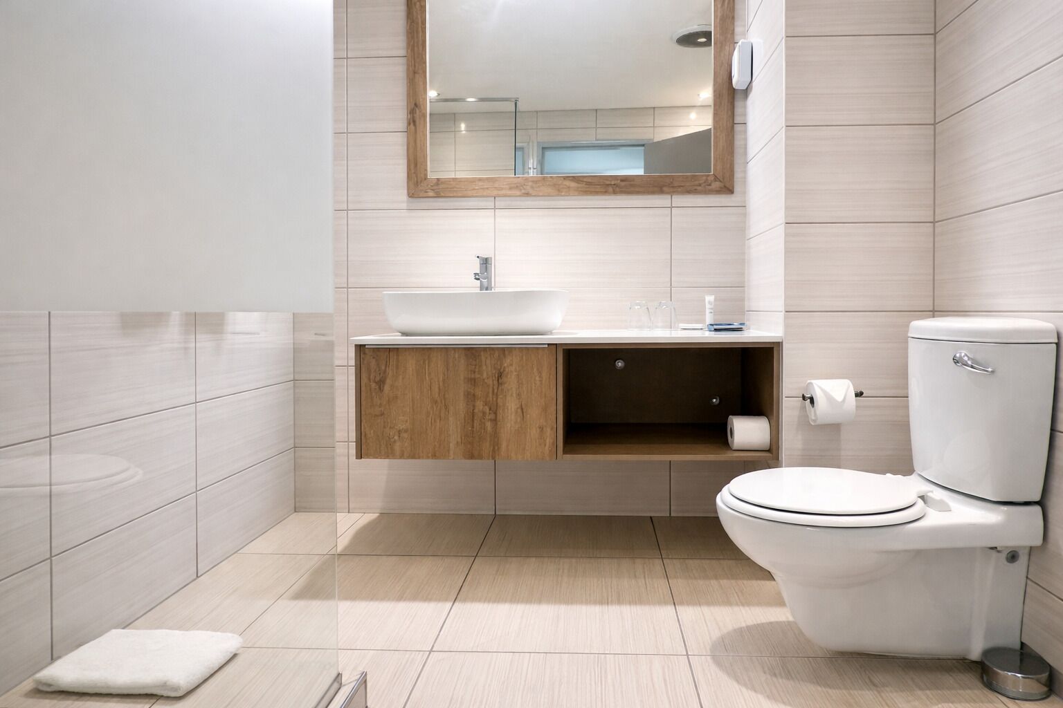 A modern bathroom with a white sink, wooden vanity, toilet, and a mirror above the sink.