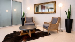 Un hall d’entrée comprenant deux fauteuils en osier, une table ronde, un grand miroir et deux lampadaires.