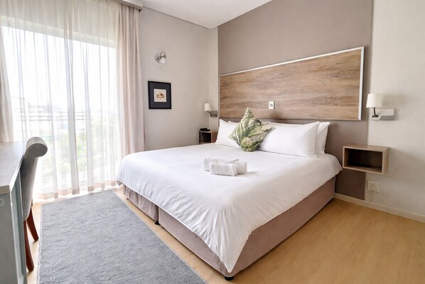 Una habitación de hotel moderna con una cama grande, un escritorio y vistas al exterior.
