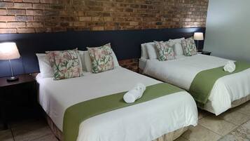 A hotel room with two beds, a brick wall, and a nightstand with a lamp.