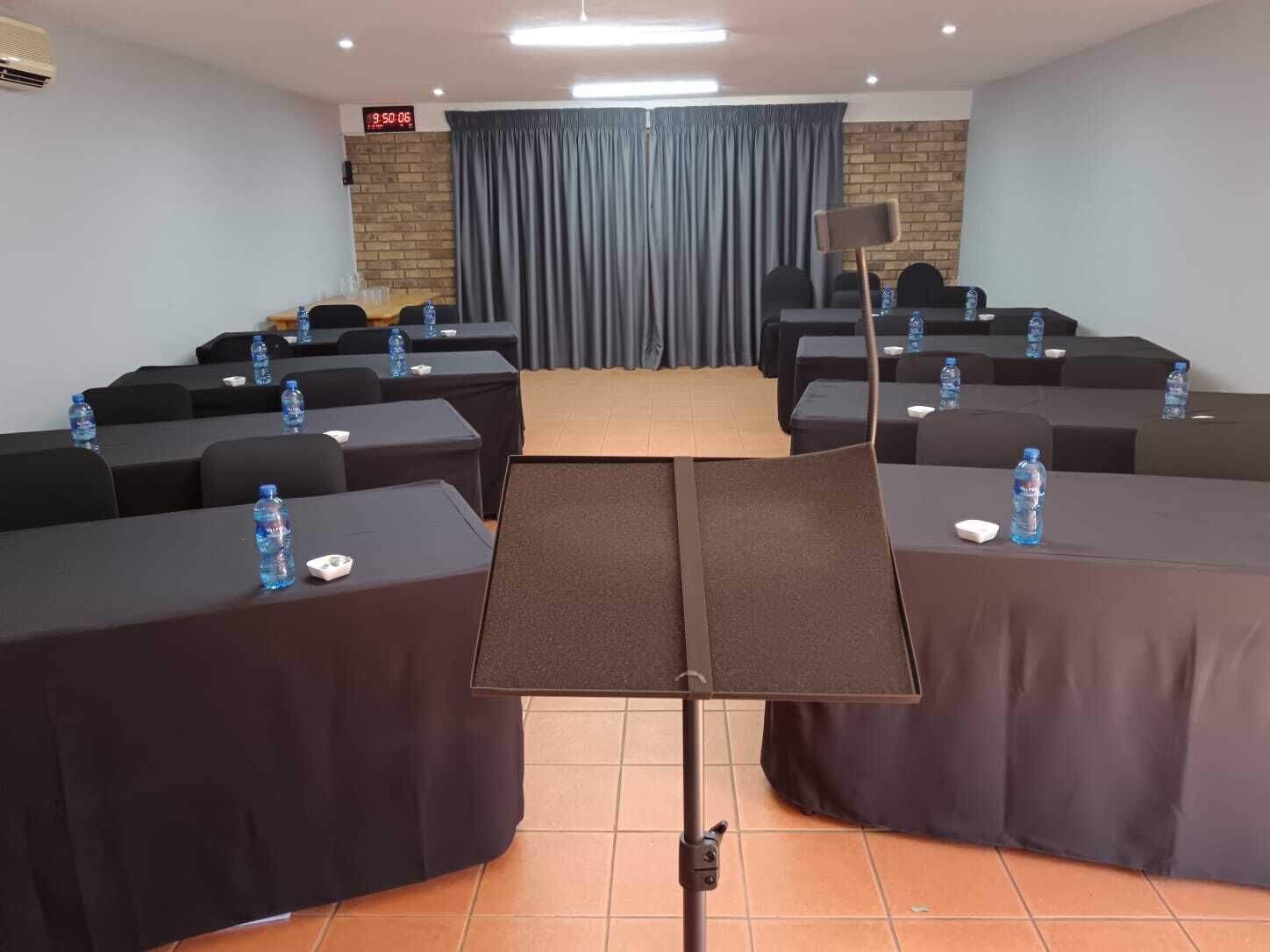 Uma sala de conferência com mesas, cadeiras, um pódio e um relógio na parede.