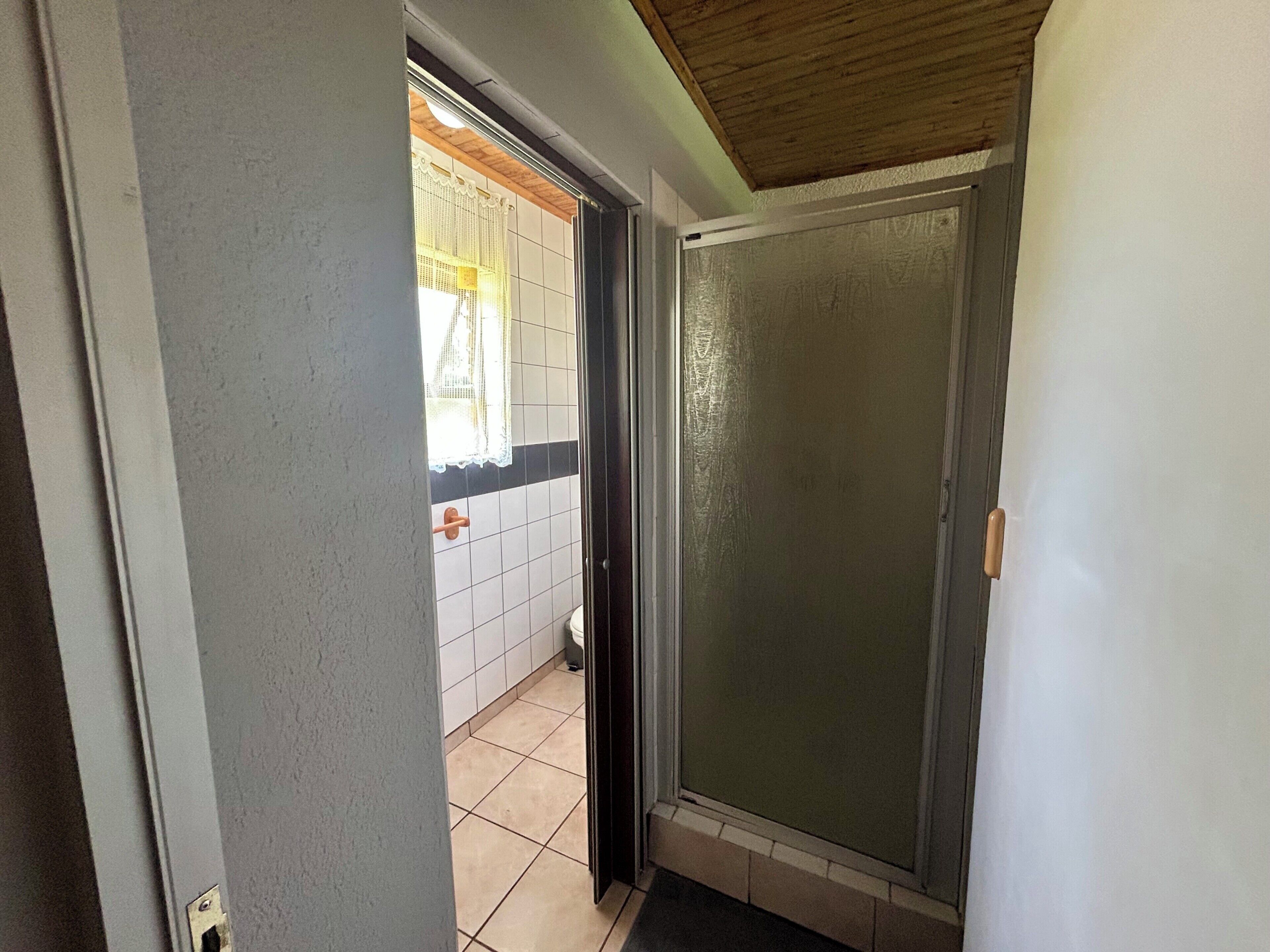 A hallway with a sliding glass door leading to a bathroom with white tiles and a wooden ceiling.