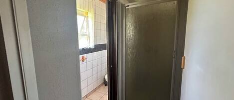 A hallway with a sliding glass door leading to a bathroom with white tiles and a wooden ceiling.