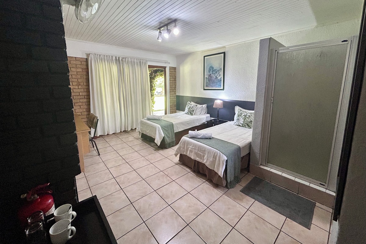 Habitación de hotel con dos camas, un escritorio, una silla, un ventilador y una ventana con cortinas.