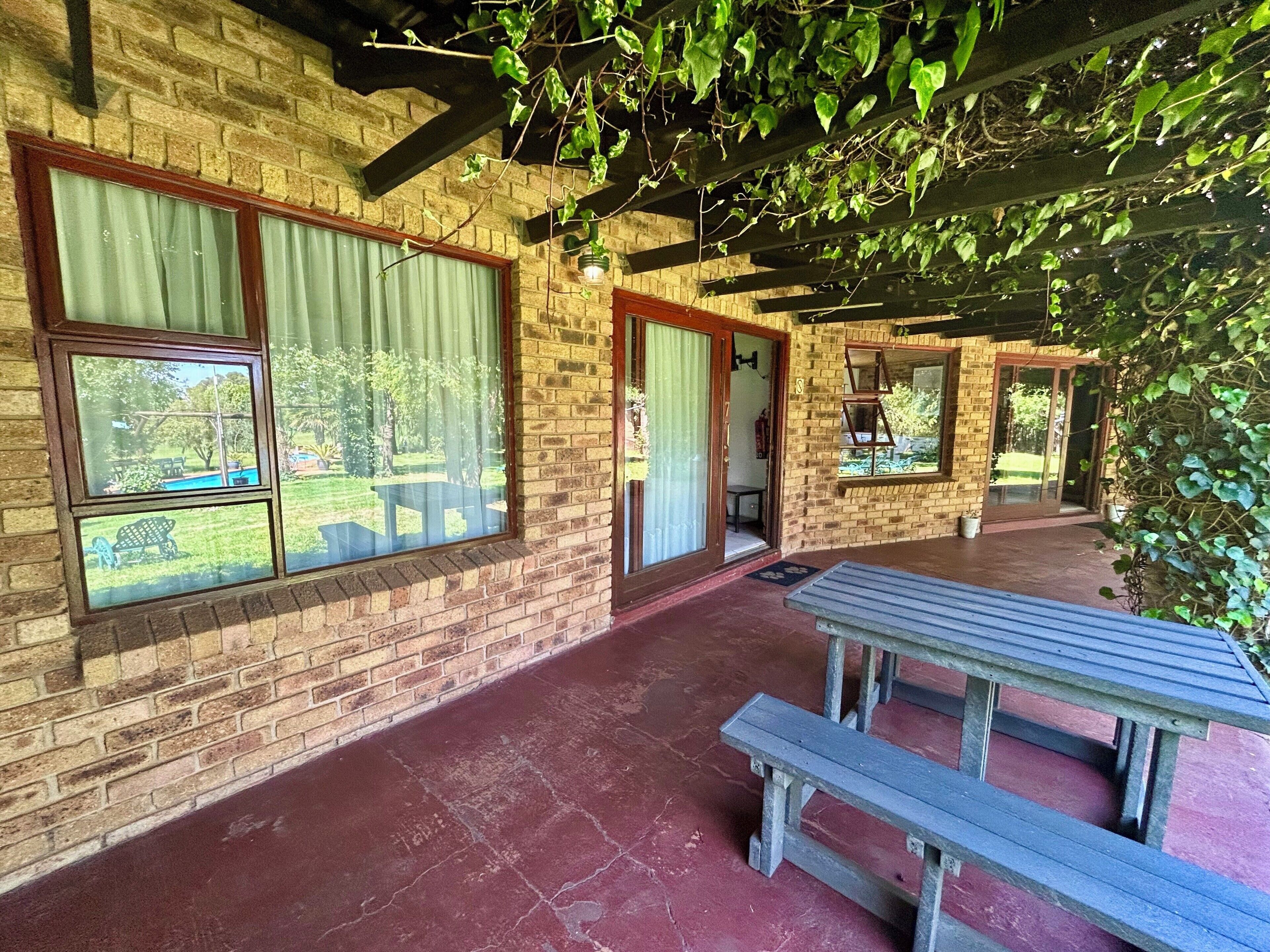 A covered patio area with brick walls, large windows, and a wooden bench.