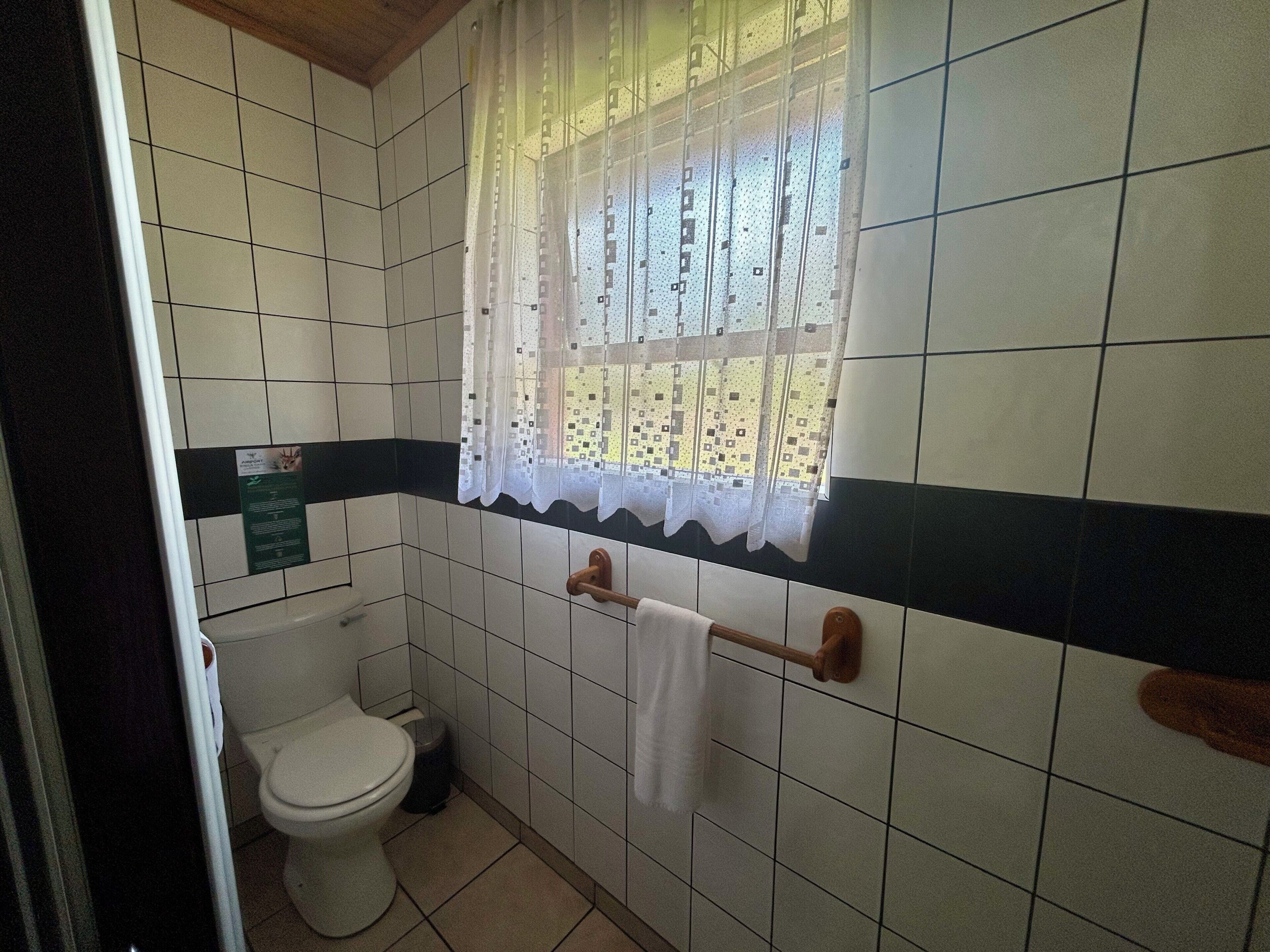 A bathroom with a toilet, a towel rack, and a window with a patterned curtain.