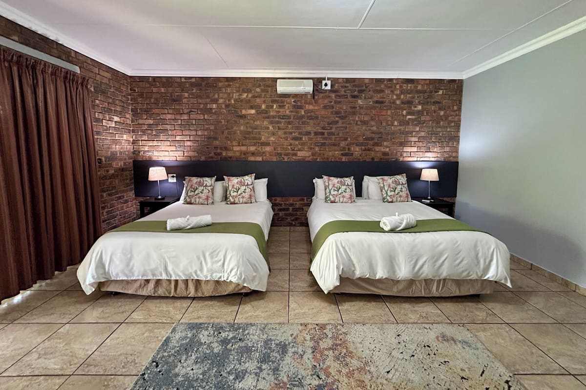 Habitación de hotel con dos camas, una pared de ladrillo, techo plano y un ventanal grande.