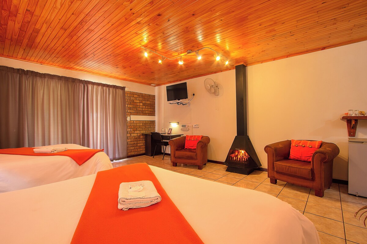 Een hotelkamer met twee bedden, een bureau, een stoel, een open haard en een aan de muur bevestigde televisie.