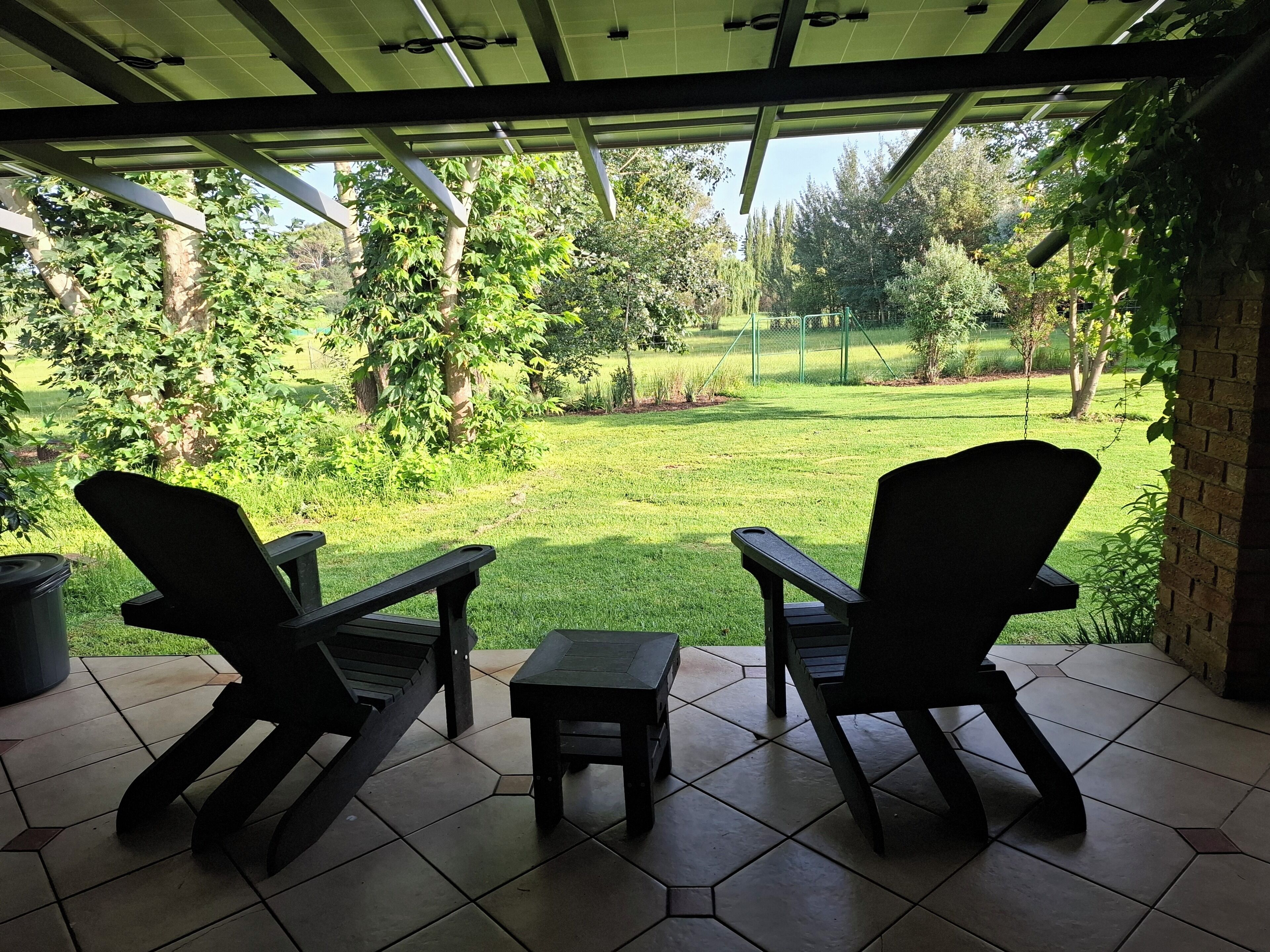 Une terrasse couverte avec deux chaises et une petite table, donnant sur un espace verdoyant agrémenté d’arbres et d’une clôture.