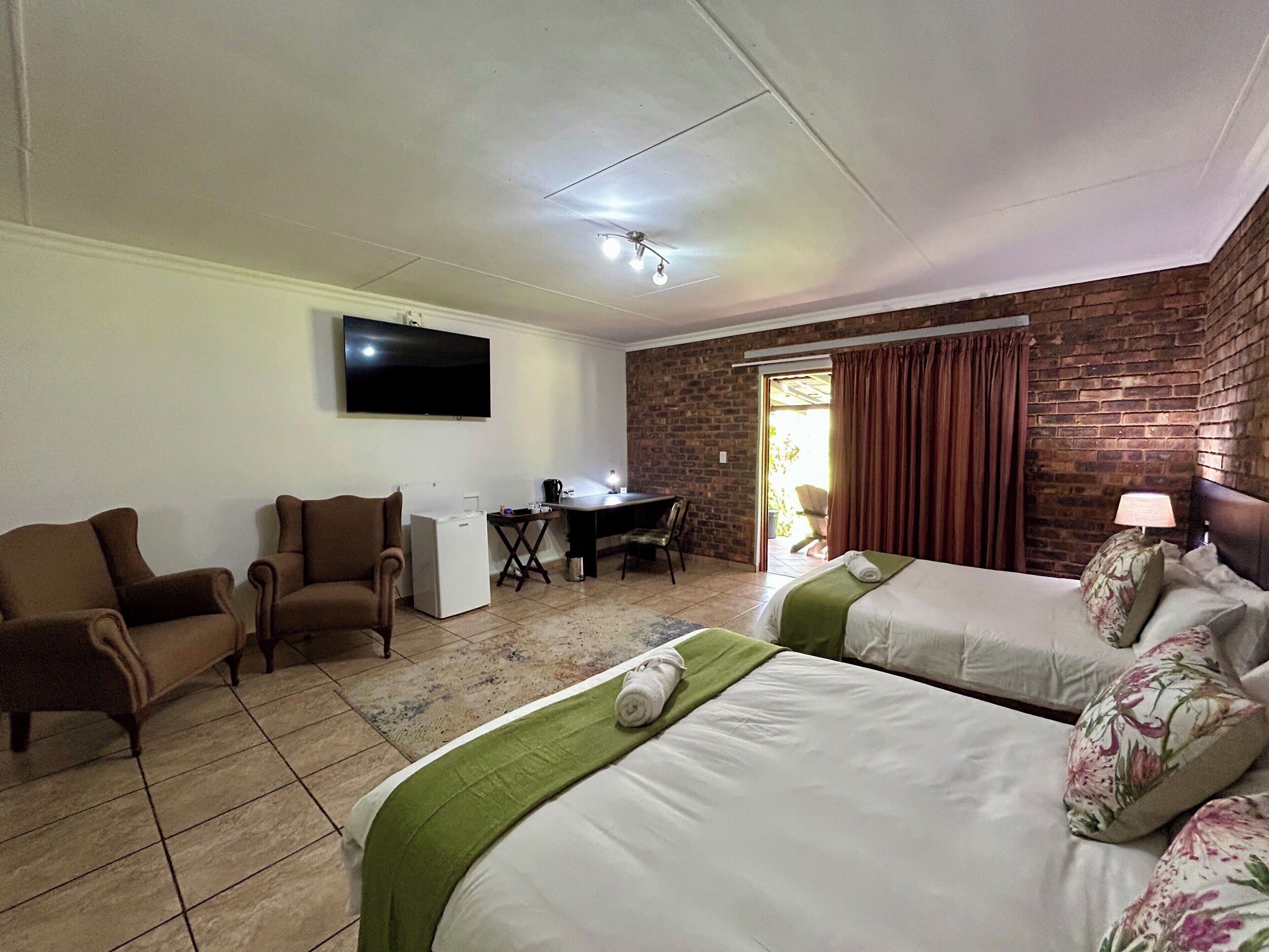 A hotel room with two beds, a desk, a chair, a television, and a brick wall.