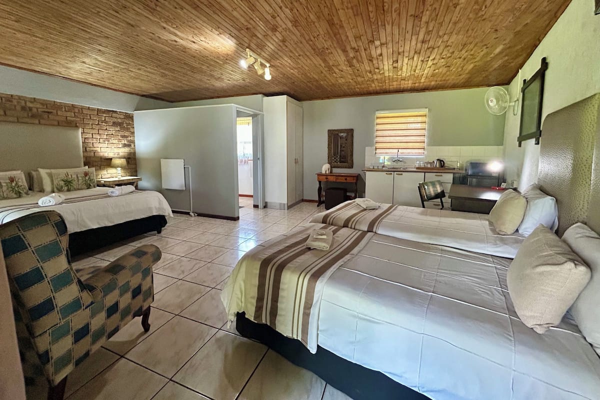 Una habitación con dos camas, un escritorio, una silla, una pequeña cocina y un baño.