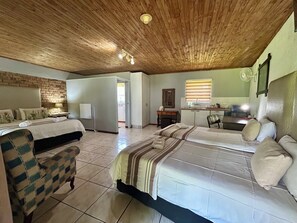 A room with two beds, a desk, a chair, a small kitchen area, and a bathroom. -  Airport Bird & Game Lodge (Kempton Park)
