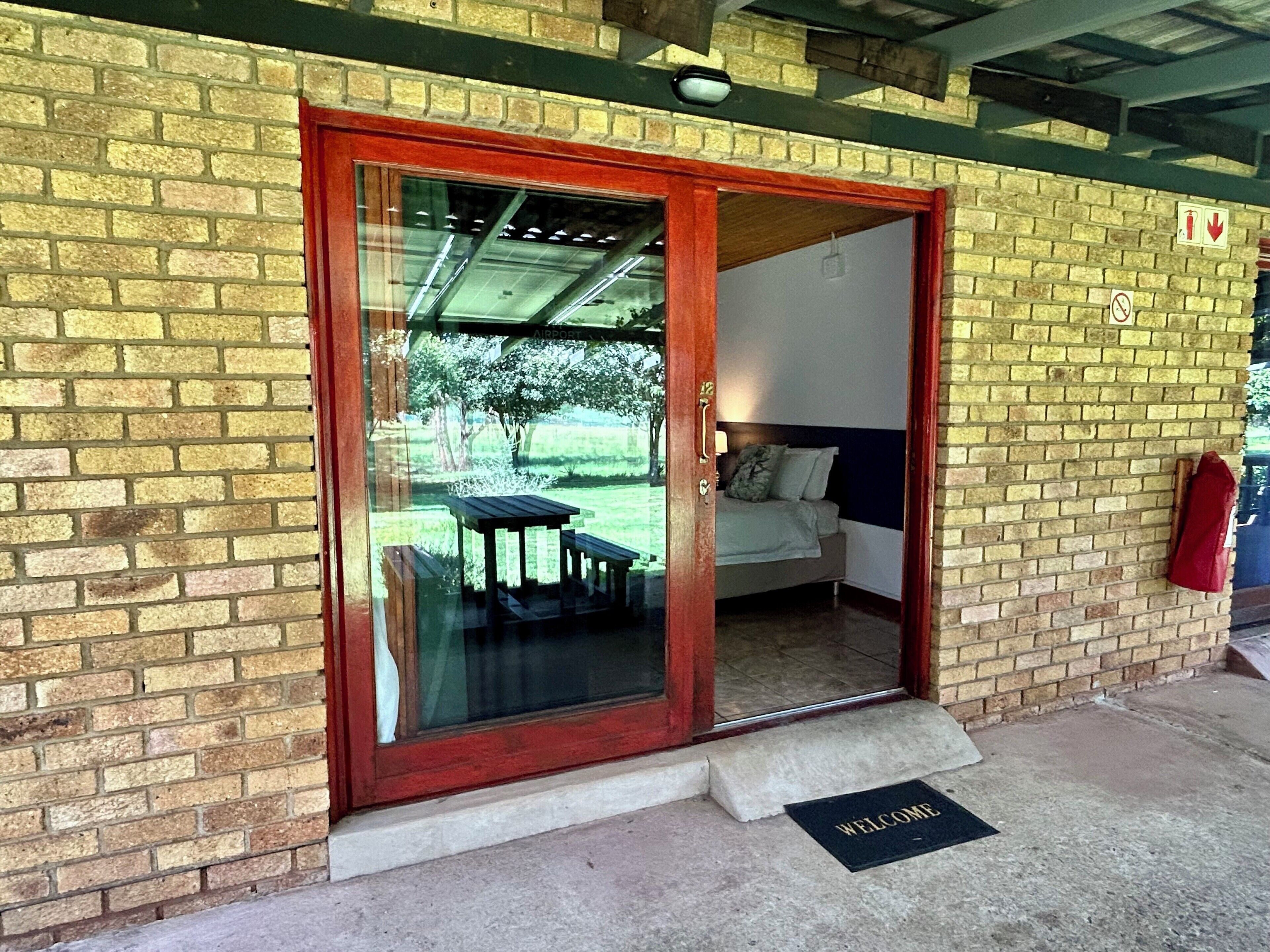 A wooden door with a glass panel, a welcome mat, and a bed visible inside.
