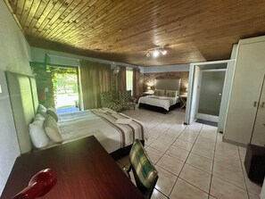 A bedroom with a bed, a chair, a table, a fan, and a wardrobe. -  Airport Bird & Game Lodge (Kempton Park)