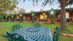 Un patio con una mesa y sillas de metal verde, rodeado de edificios de ladrillo con muros cubiertos de hiedra y zonas de estar al aire libre.