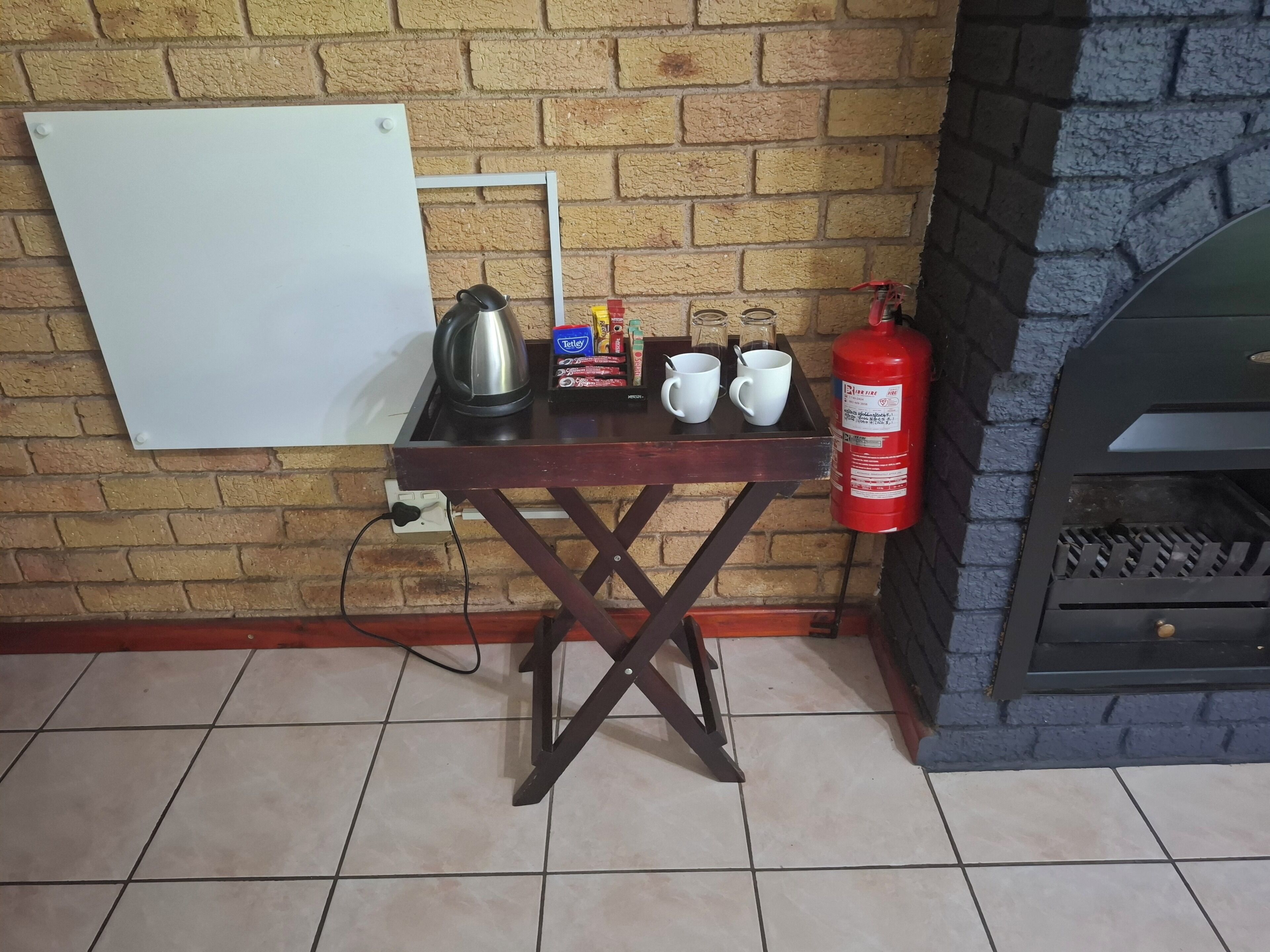Een bakstenen muur met een whiteboard, een tafel met een waterkoker, bekers, kruiden en een brandblusser.