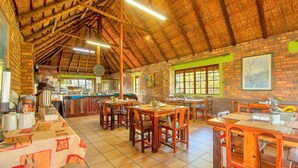 Un comedor rústico con mesas y sillas de madera, pared de ladrillo y techo de paja.