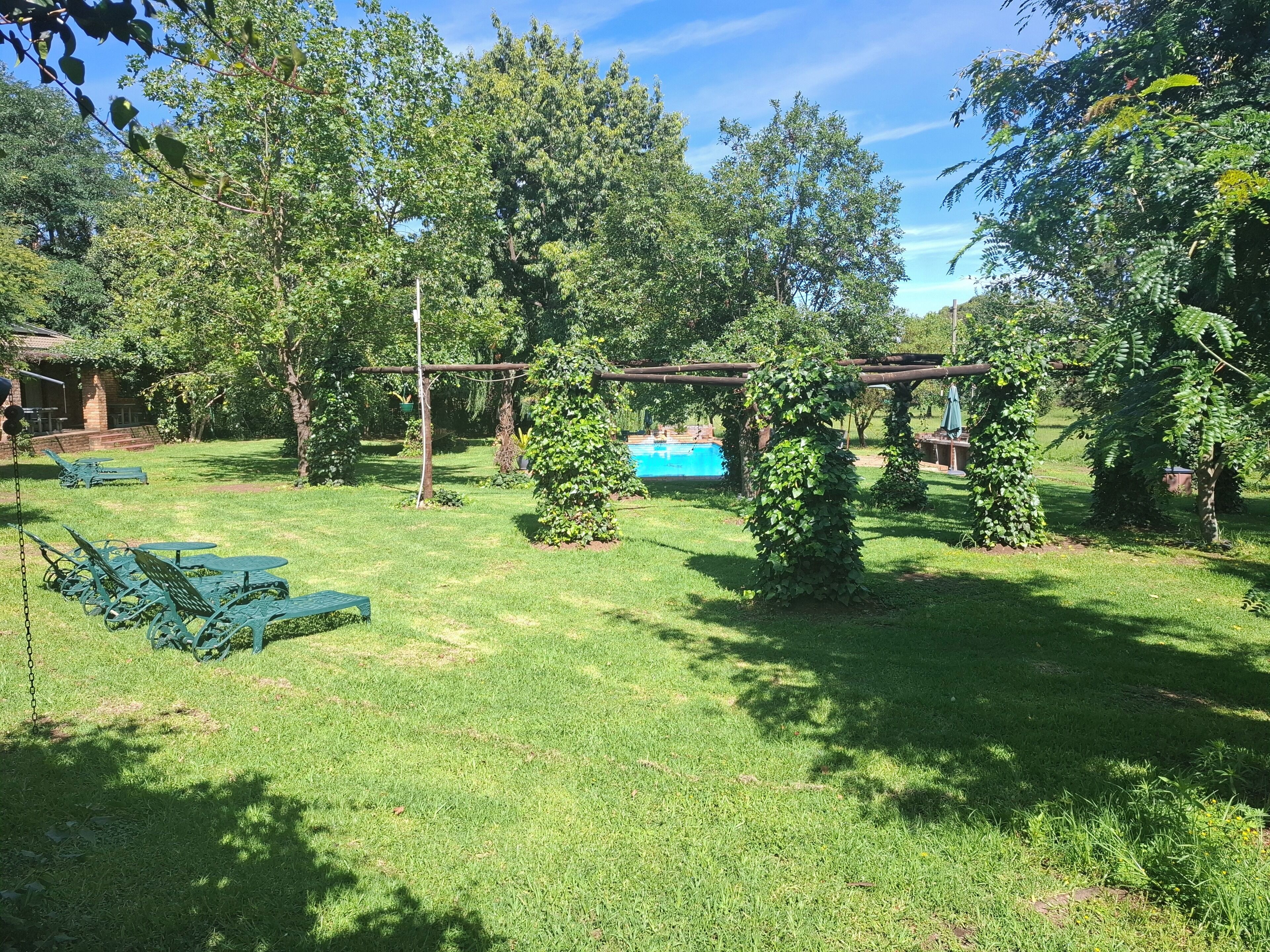 Un patio trasero con piscina, césped verde y sillas de metal.