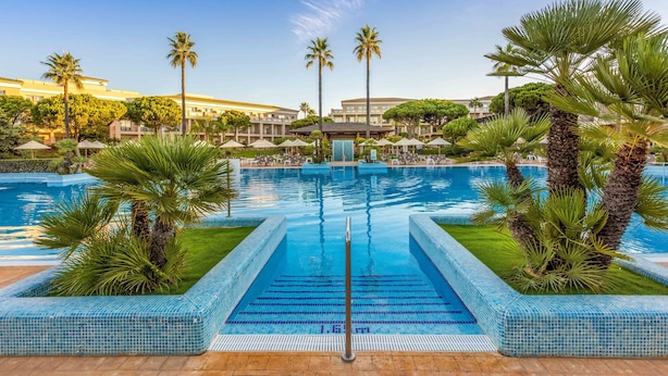 A swimming pool with palm trees and a clear blue sky. - Valentin Sancti Petri (Chiclana de la Frontera)