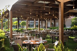 An outdoor dining area with multiple tables and chairs, arranged under a wooden pergola with hanging lights. - Valentin Sancti Petri (Chiclana de la Frontera)