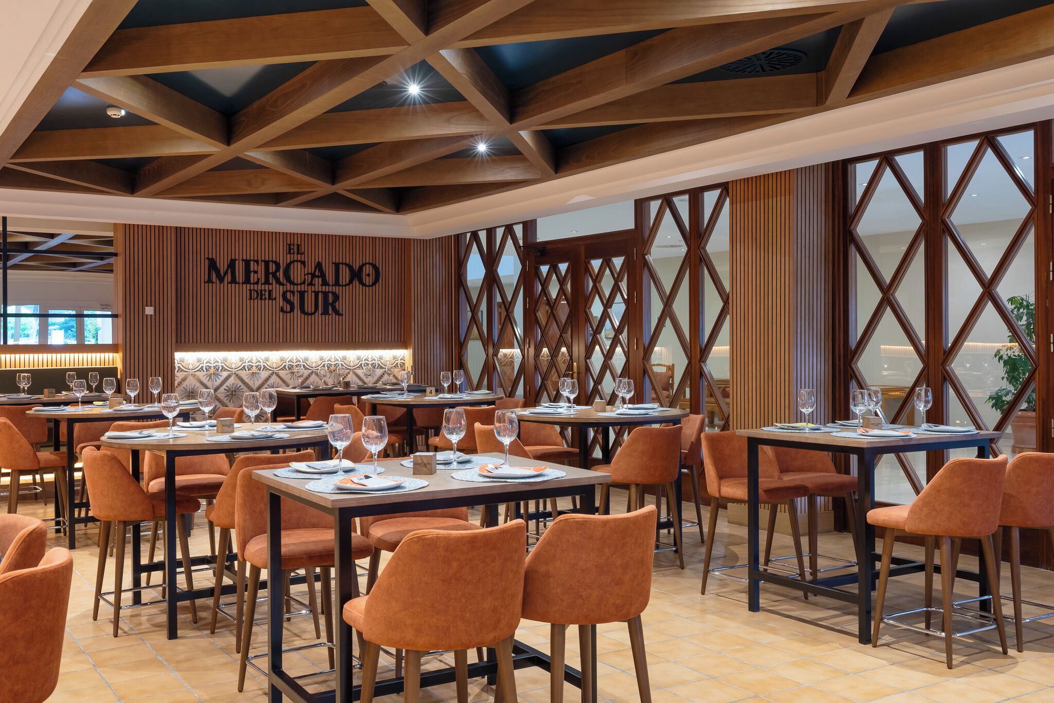 A restaurant with multiple tables and orange chairs, a wooden ceiling, and a sign reading "El Mercado del Sur".