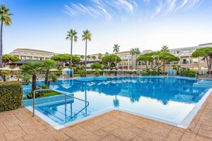 A large outdoor swimming pool with clear blue water, surrounded by palm trees and a modern building in the background. - Valentin Sancti Petri (Chiclana de la Frontera)