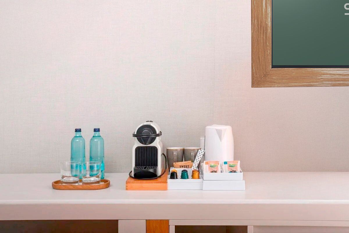 Minibar de una habitación de hotel con una cafetera, dos botellas de agua, un vaso y una bandeja con diversos artículos.