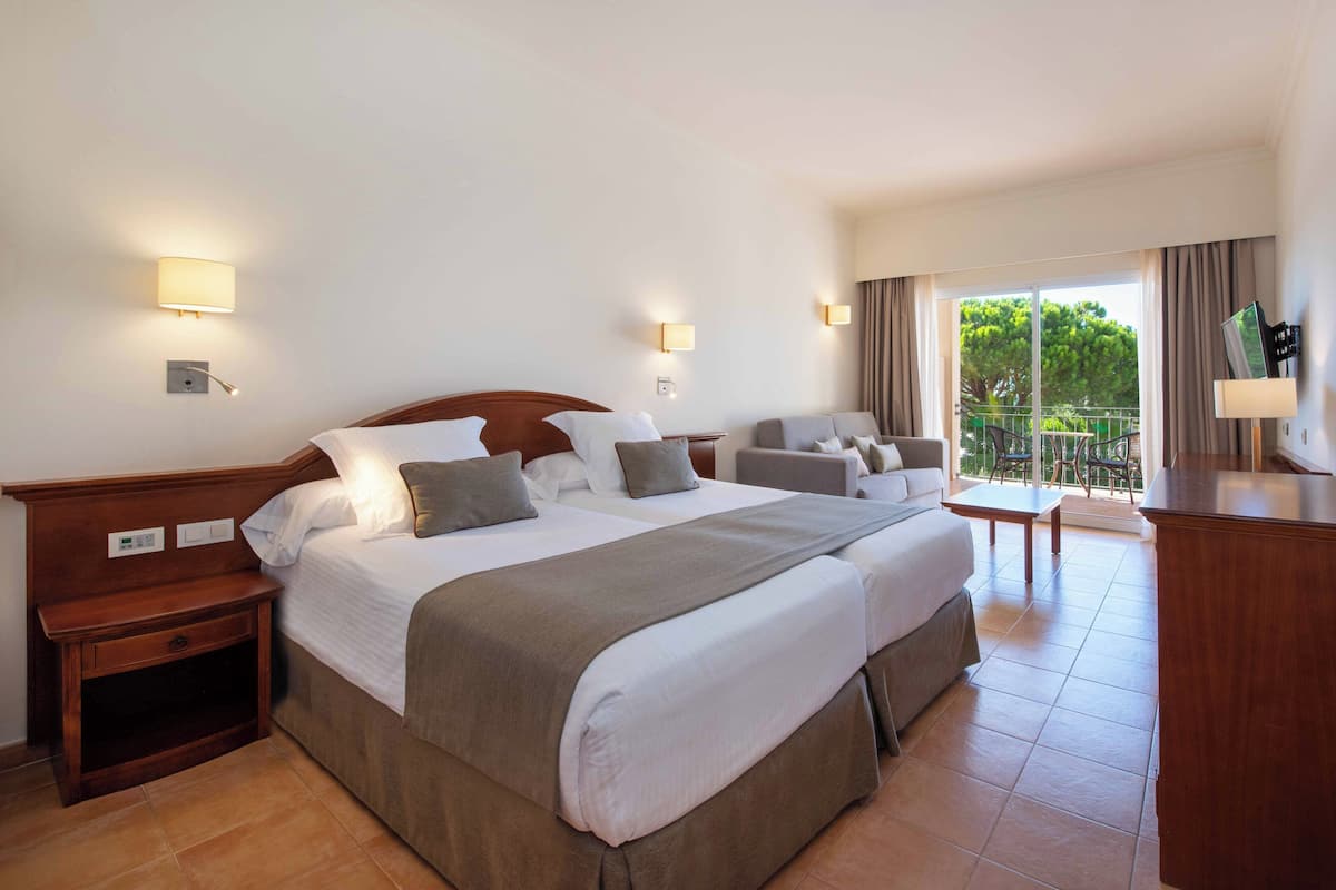 A hotel room with a large bed, two bedside tables, a desk, and a balcony with a view.