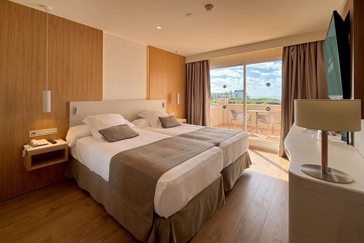 A hotel room with a large bed, a desk, a chair, and a balcony with a view.