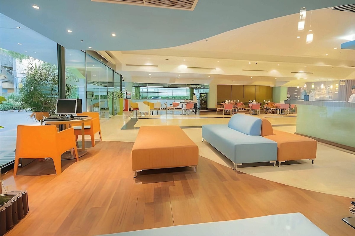 Een moderne hotel lobby met houten vloeren, zithoeken en een groot raam met uitzicht op de omgeving.