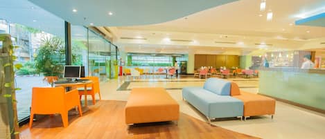 Un moderno vestíbulo de hotel con suelo de madera, un mostrador de recepción, zonas de estar y grandes ventanales con vistas al exterior.