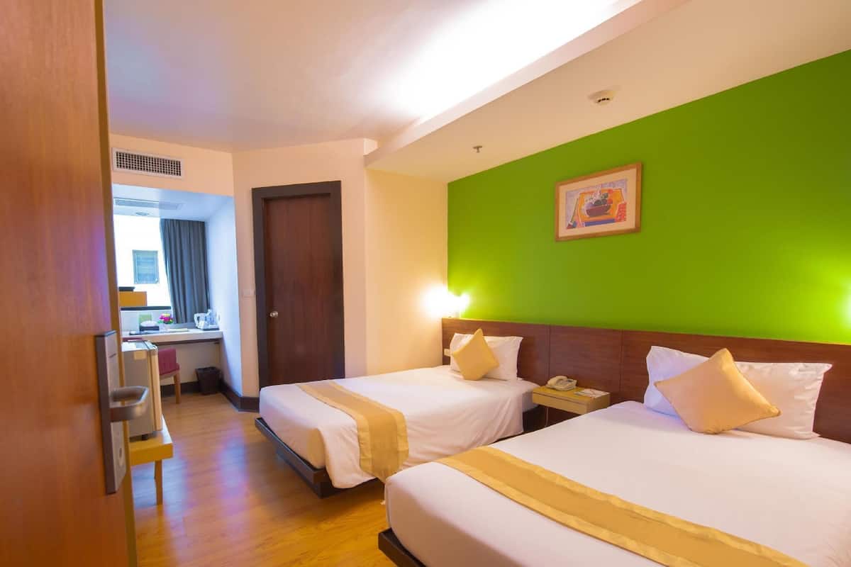 A hotel room with two beds, a green wall, and a wooden floor.