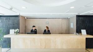 A reception desk with two staff members, a clock, and a plant. - Seasons Siam Hotel (Bangkok)