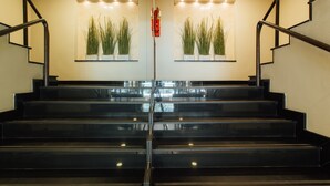 A set of black stairs with glass railings, leading to a landing with two wall-mounted planters with green plants. - Seasons Siam Hotel (Bangkok)