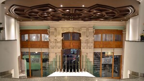 Un hall d’entrée doté d’un escalier central, d’un plafond décoré et de portes en verre avec des panneaux indicateurs.