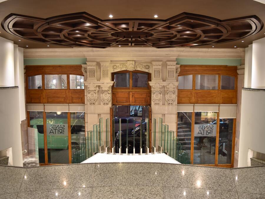 Eine Lobby mit einer zentralen Treppe, einer verzierten Decke und Glastüren mit Beschilderung.