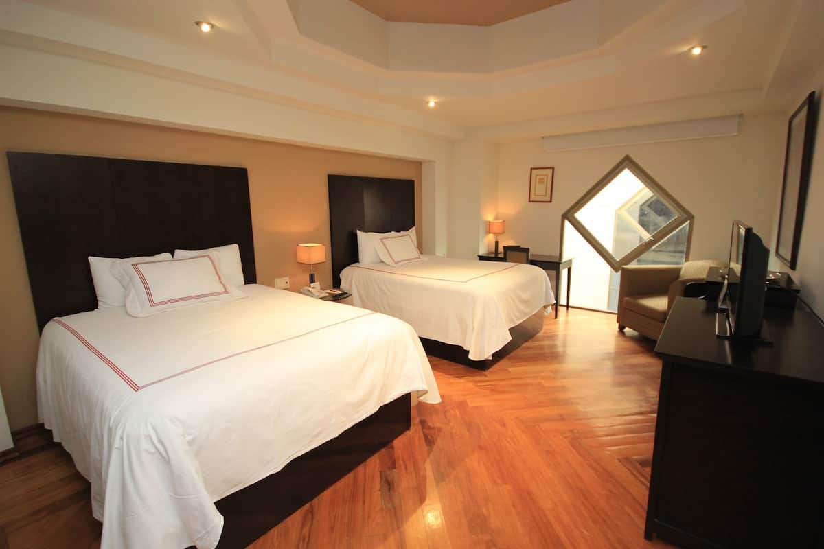 Une chambre d’hôtel avec deux lits, un bureau, une chaise et une grande fenêtre.