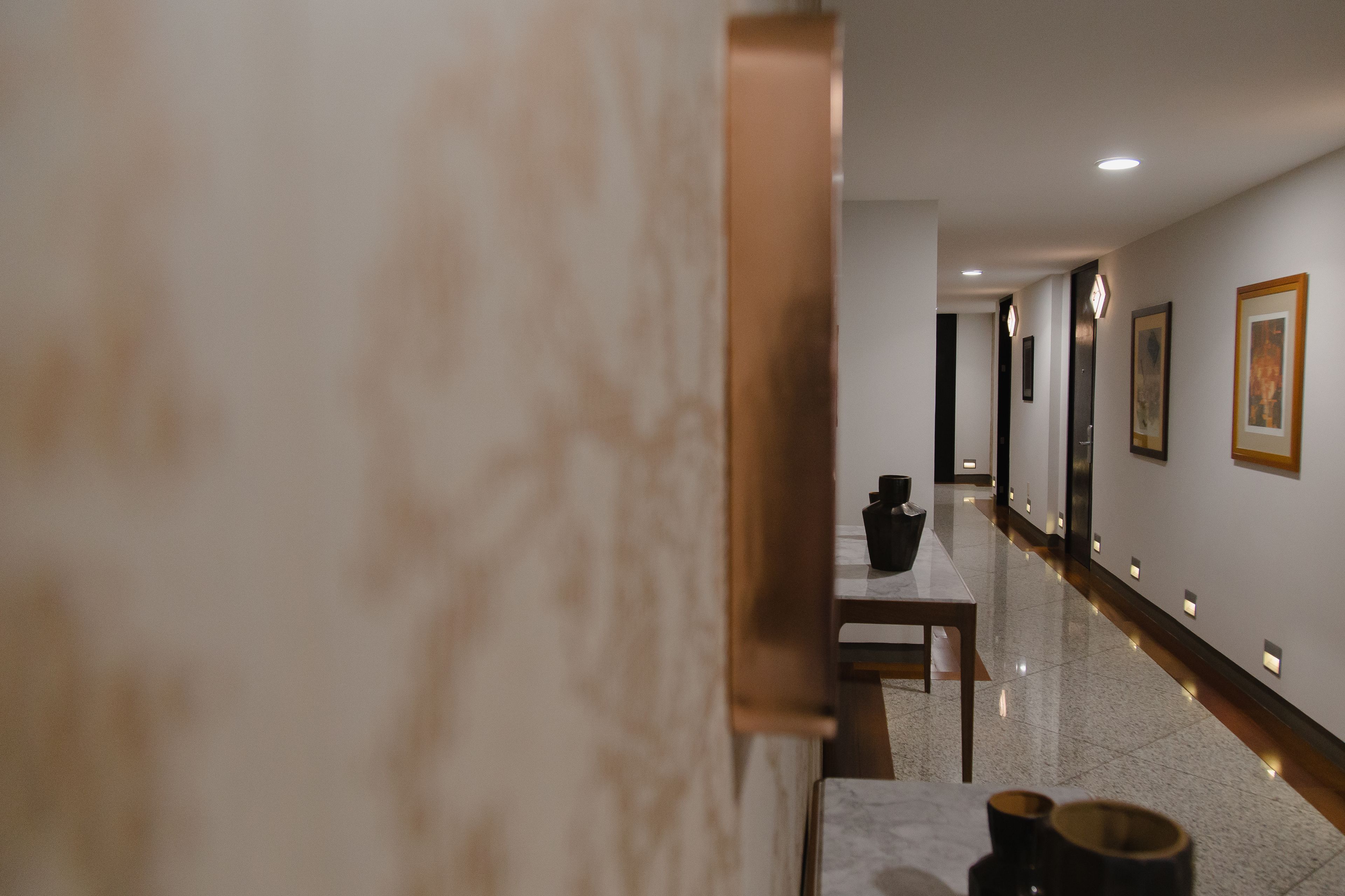 A hallway with a marble wall, a wooden table, and a black vase.