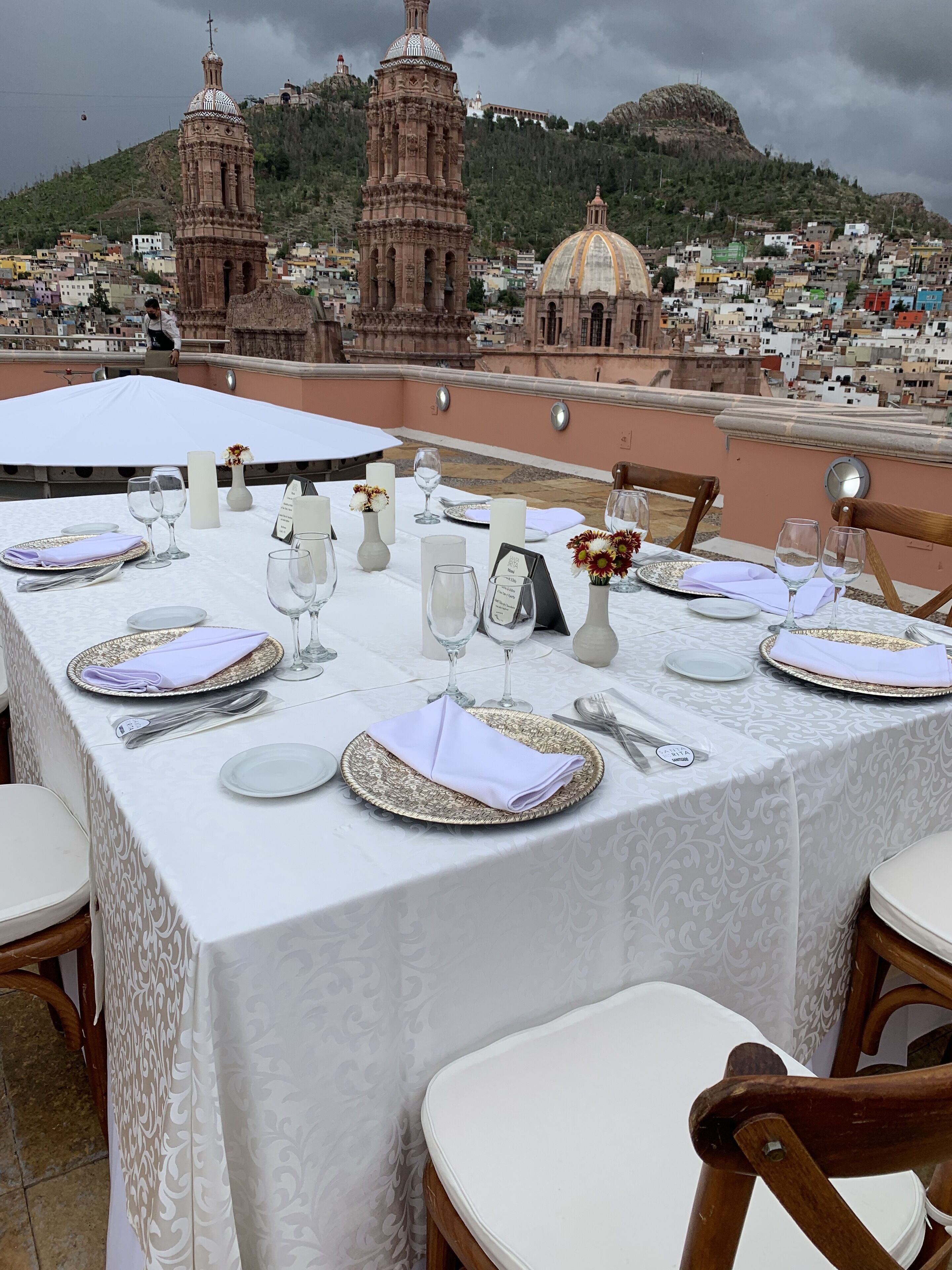 Mesa preparada para comer con vista a la ciudad, incluyendo torres históricas y una colina.