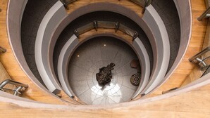 Un escalier en colimaçon orné d’une sculpture centrale, entouré d’une plateforme circulaire dont le sol est recouvert de carreaux.