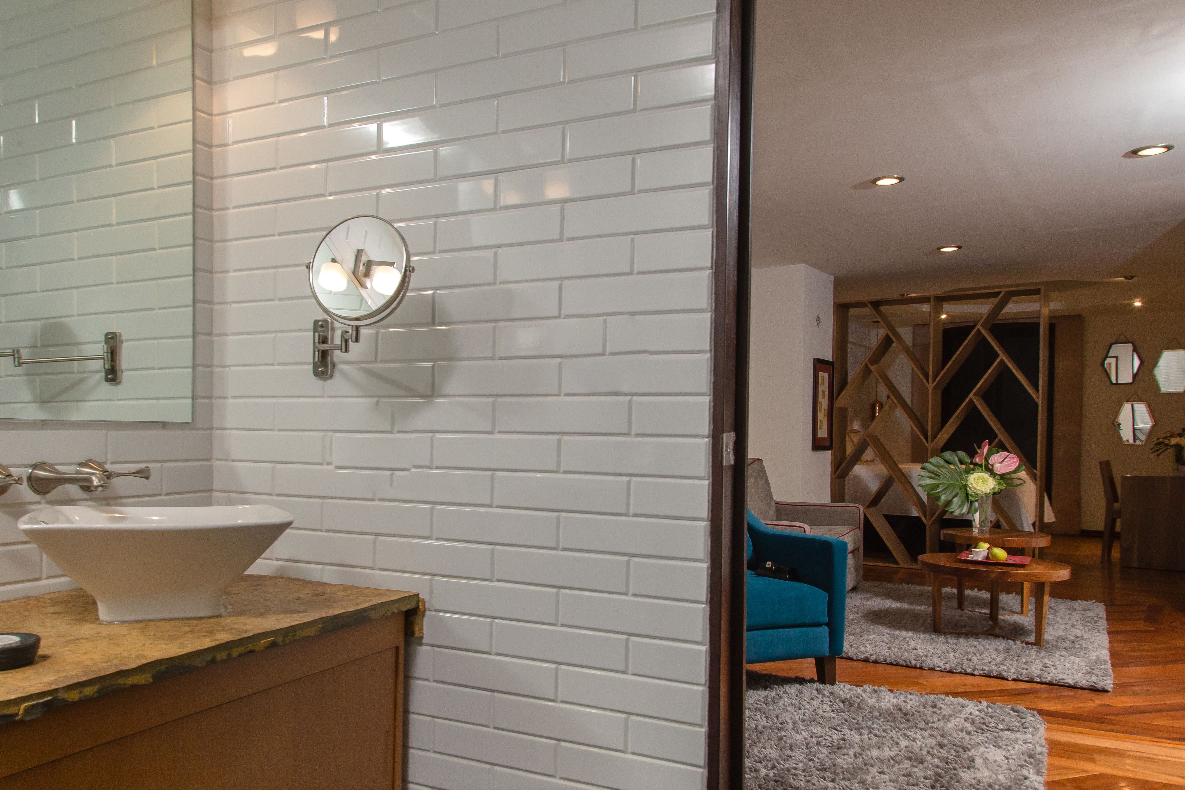Un baño moderno con azulejos blancos tipo metro, un espejo redondo y un lavabo blanco.