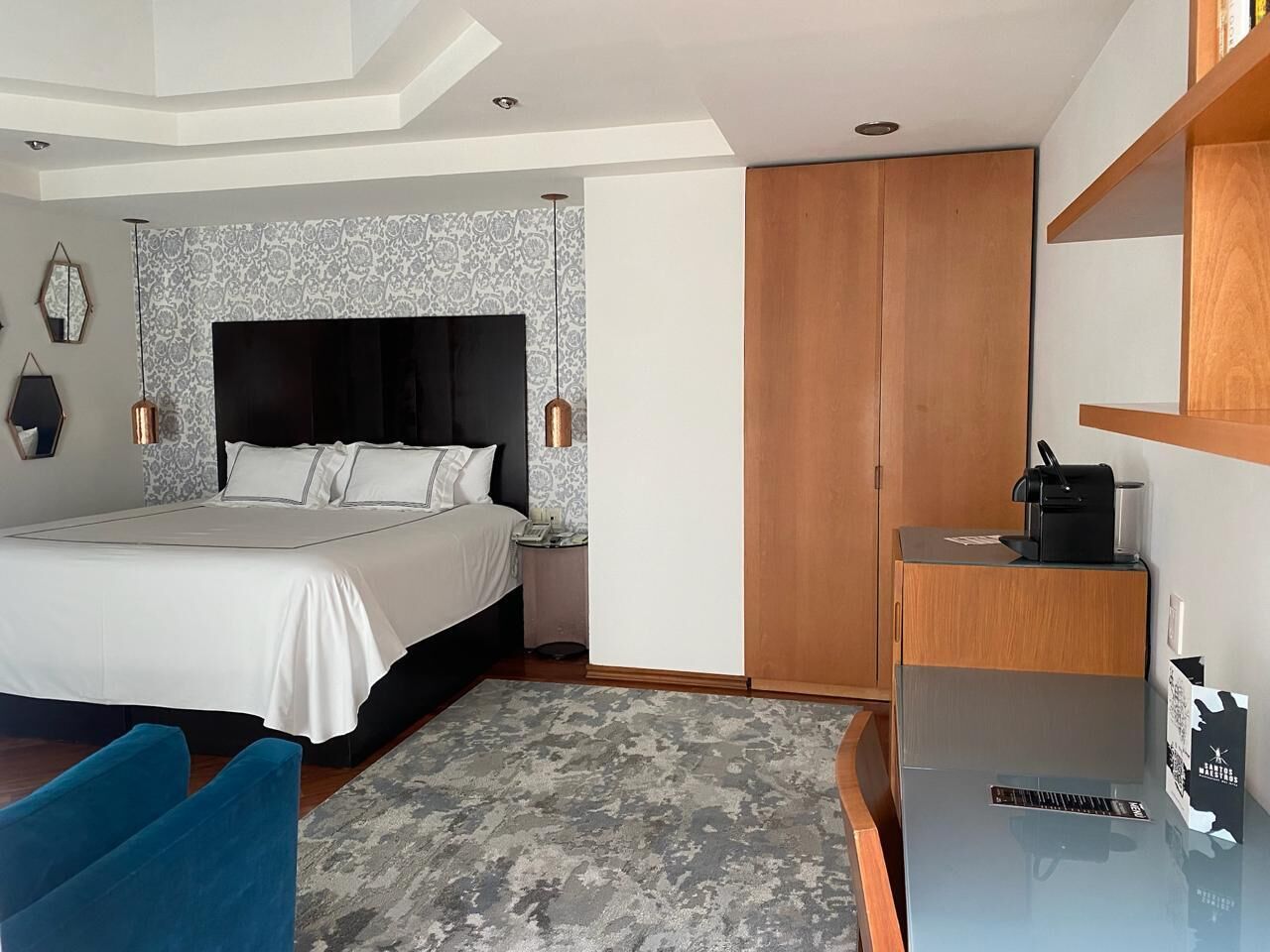 Una habitación de hotel moderna con una cama grande, un escritorio con cafetera y un armario.