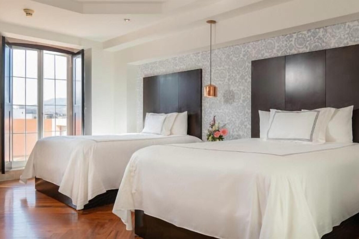 A hotel room with two beds, a large window, and a view of the outdoors.