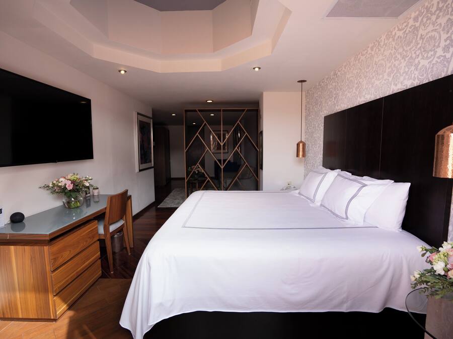 A bedroom with a large bed, a desk with a chair, a flat-screen TV, and a decorative wall panel.