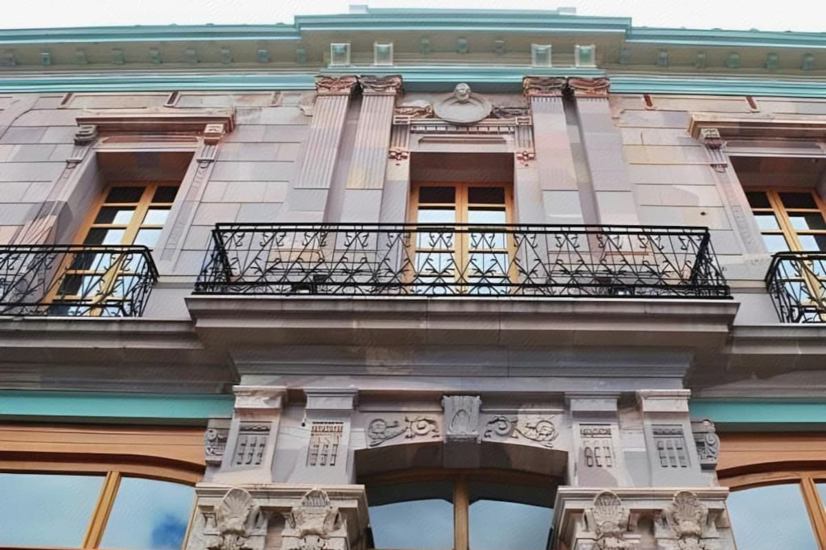 A building facade with ornate architectural details, including a balcony with metal railings and a central decorative archway.