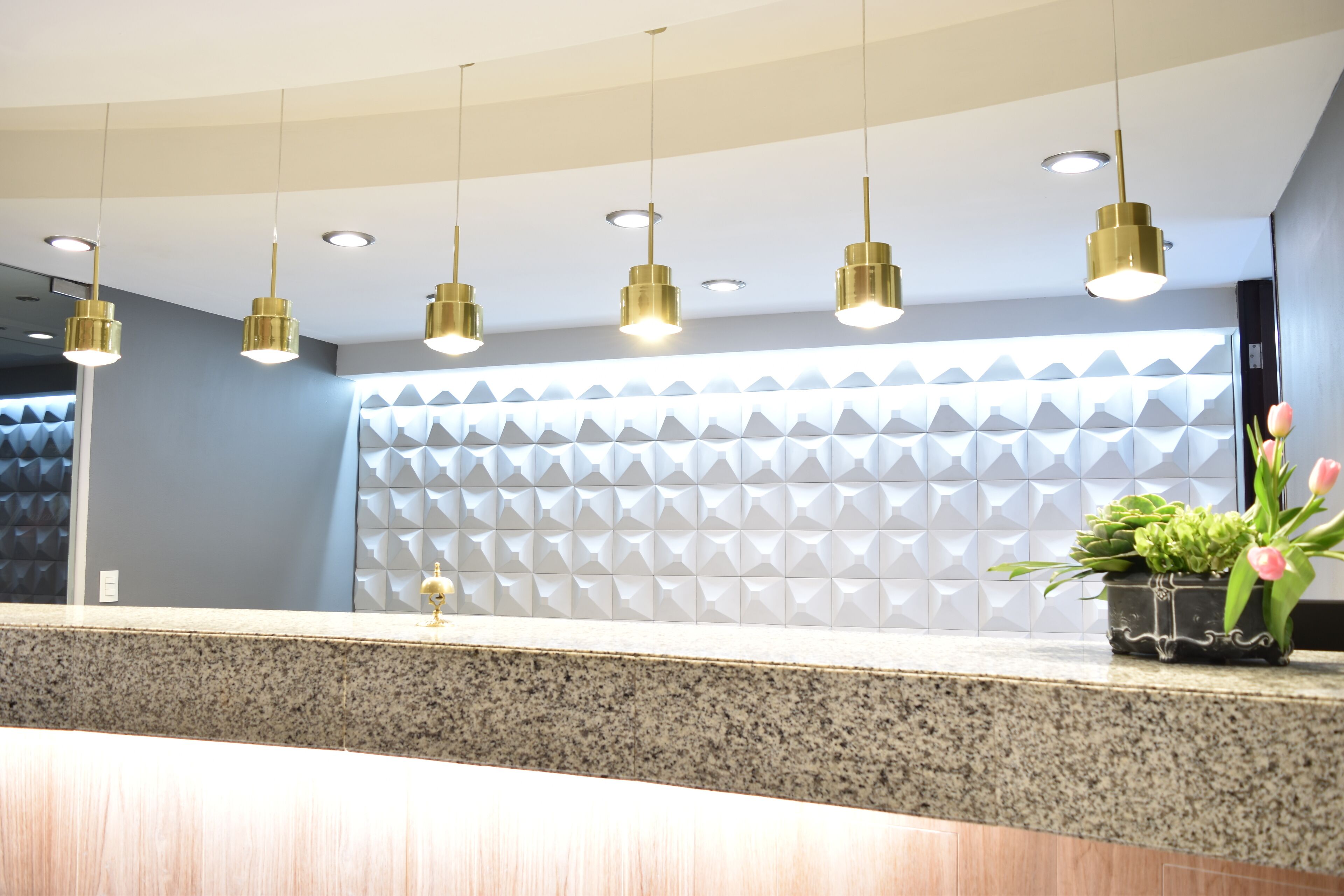 Un área de recepción con mostrador de granito, iluminación colgante dorada y un diseño de pared geométrico.