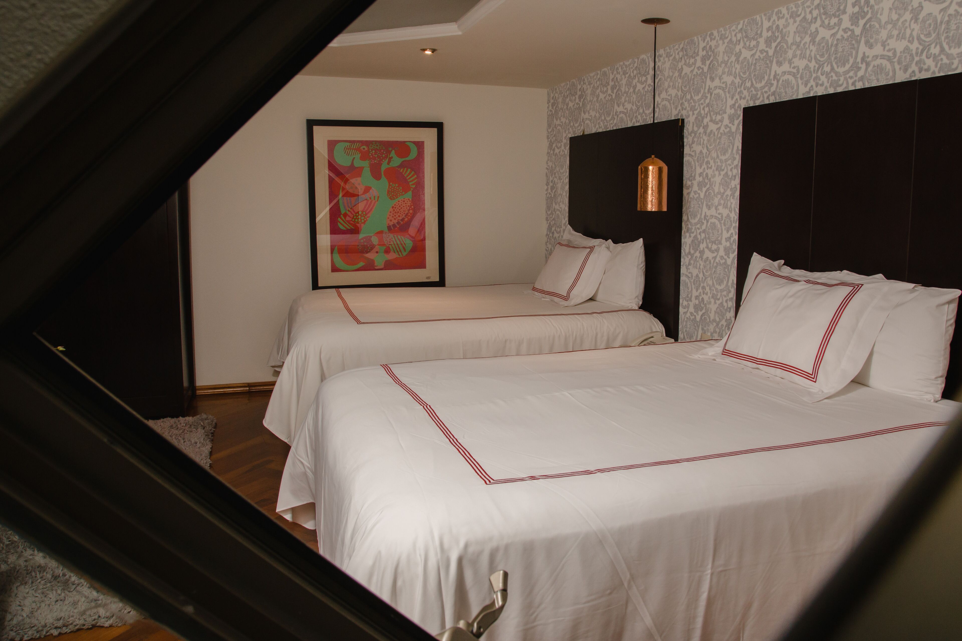A hotel room with two beds, a framed artwork on the wall, and a pendant light.
