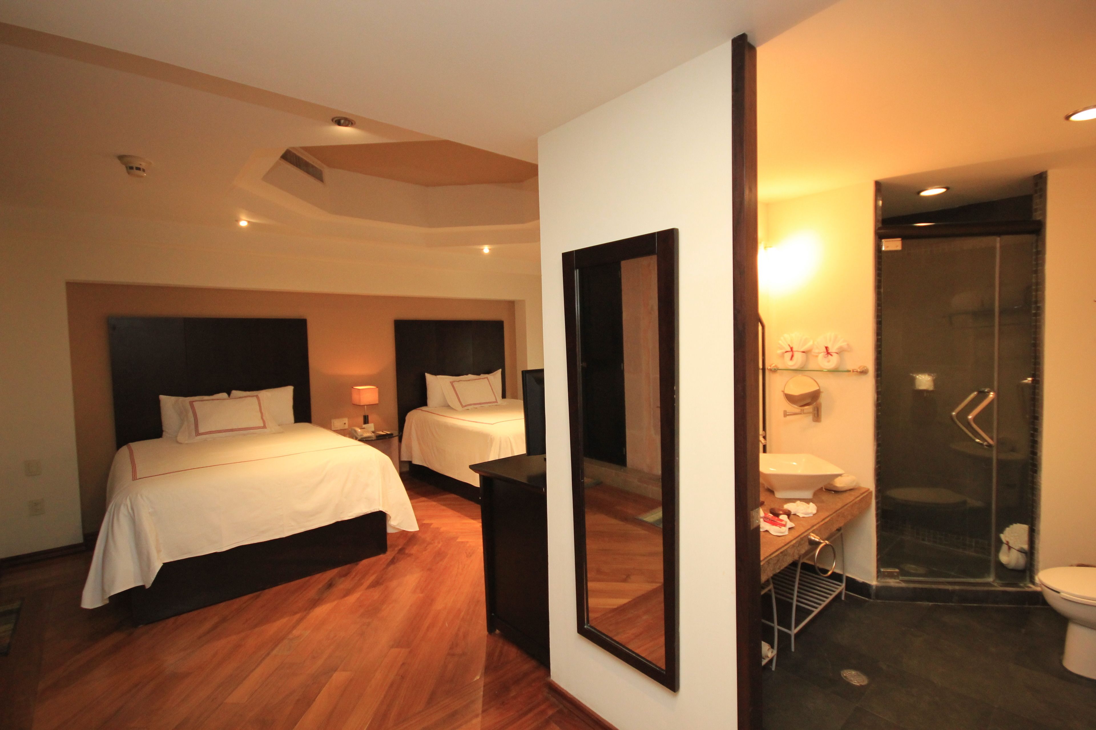 Habitación de hotel con dos camas, un espejo grande, baño con ducha y lavamanos.